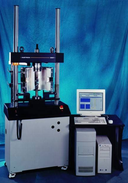 | Instron Industrial material testing machine with vertical columns and clamp setup, connected to a desktop computer on a blue backdrop.