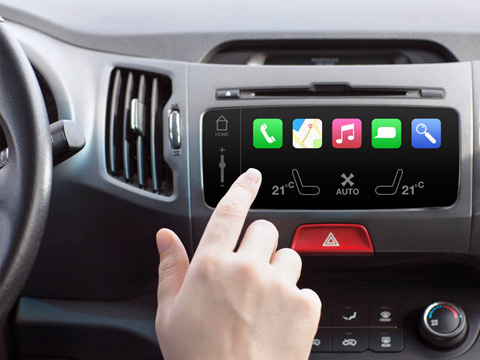 Close-up of a hand tapping a car's touchscreen infotainment system with app icons (Phone, Maps, Music, Messages) and climate controls visible below.