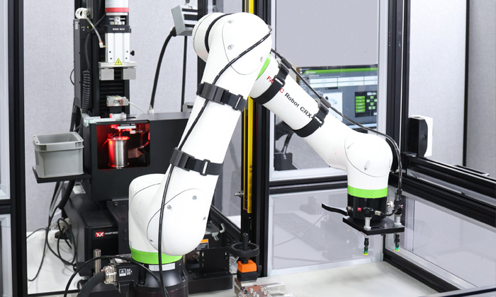 | Instron Bras de robot collaboratif s’étendant à travers une cellule d’essai automatisée pour saisir une éprouvette en vue d’essais mécaniques sur un système d’essai universel Instron 68SC