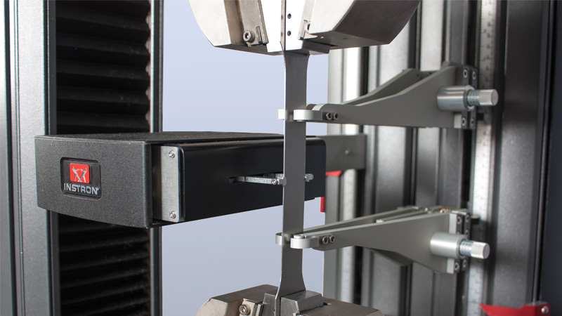 | Instron Dünne Metallprobe, befestigt in Keilspannbacken an einem Instron Universalprüfsystem, mit dem Instron AutoXBiax Extensometer für die biaxiale Dehnungsmessung während des Zugversuchs