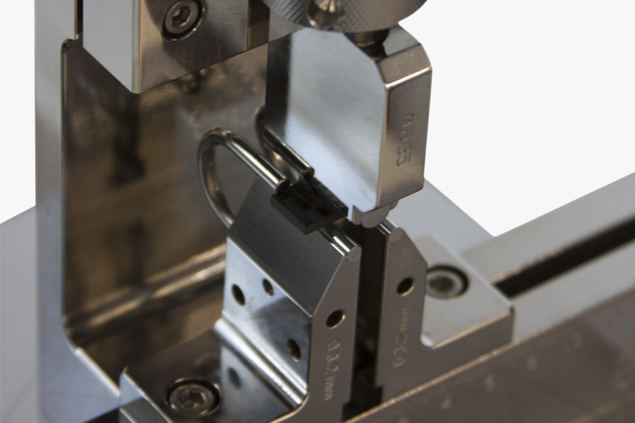 | Instron Extreme close-up of specimen stops on an Instron interlaminar shear strength test fixture, with a composite laminate specimen precisely positioned between the fixture components