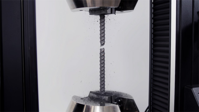 | Instron Close-up of a steel rebar specimen undergoing tensile failure between hydraulic wedge grips on an Instron 68FM universal testing machine, with debris particles visible at the point of fracture