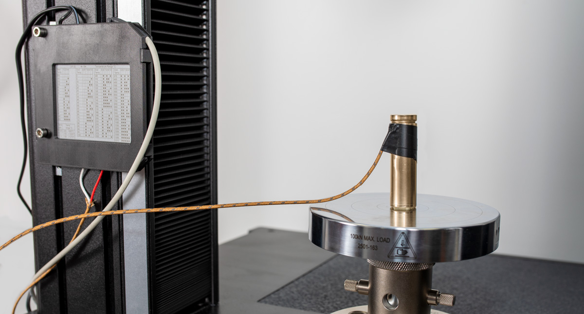 | Instron Capteur câblé connecté à une éprouvette de pile cylindrique sur un système d’essai Instron pour capturer les données de tension synchronisées avec un essai de compression.