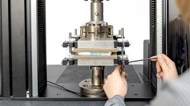 Technician positioning a battery pouch cell component between compression platens on a 6800 Series 68TM table model for mechanical compression testing. | Instron