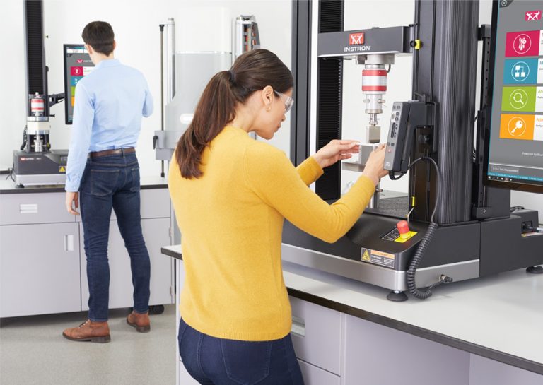 Lab technician loading a plastic specimen into flexure fixtures on an Instron 68TM table model universal testing system, with the Bluehill Universal software operator dashboard in view.