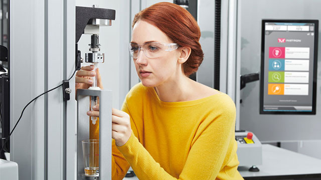 A universal syringe fixture mounted on an Instron testing system performs precision mechanical testing to evaluate syringe and injection device performance, reliability, and quality under controlled laboratory conditions.