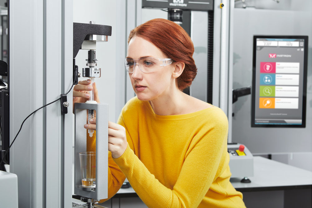 A laboratory technician operates a materials testing machine to evaluate the mechanical performance, durability, and reliability of an injection device under controlled testing conditions. | Instron