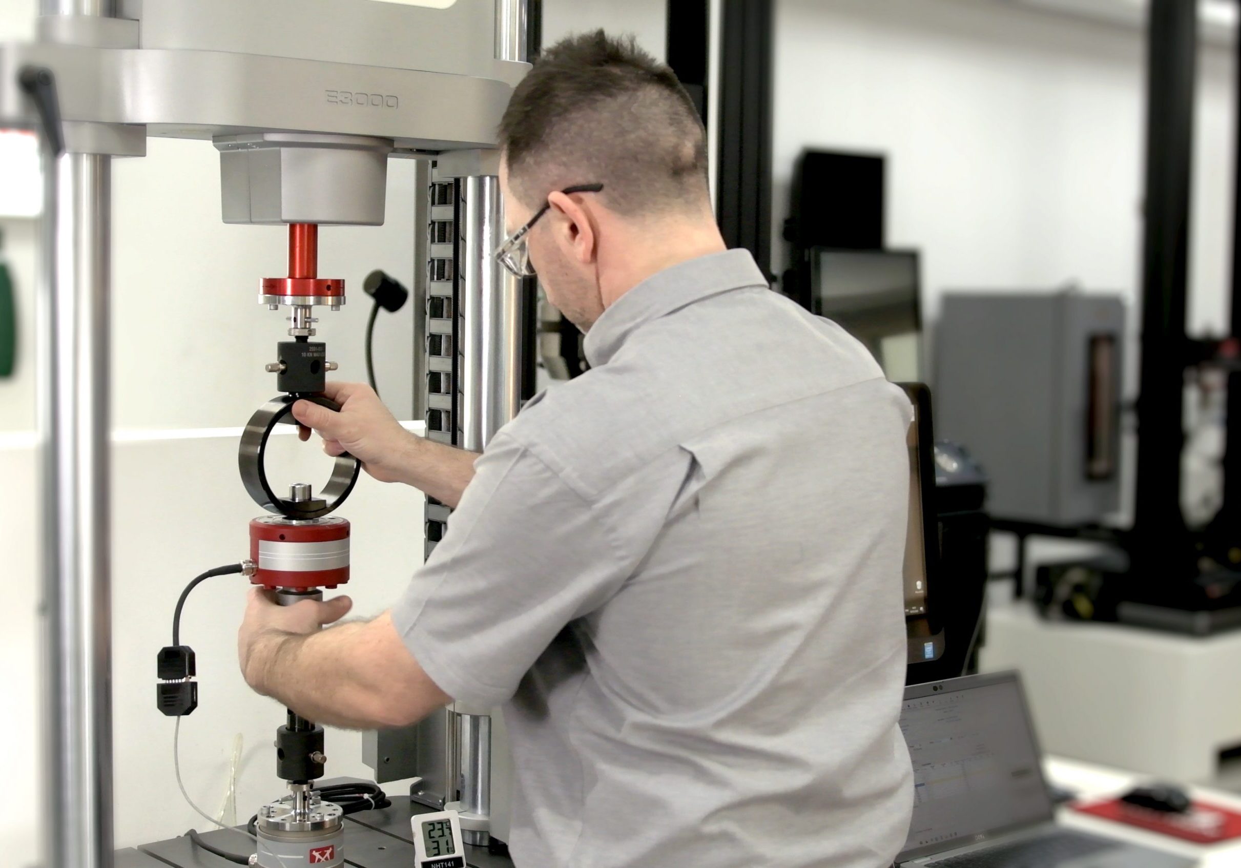 Instron field service engineer using a control panel while setting up a force calibration fixture in a testing machine.