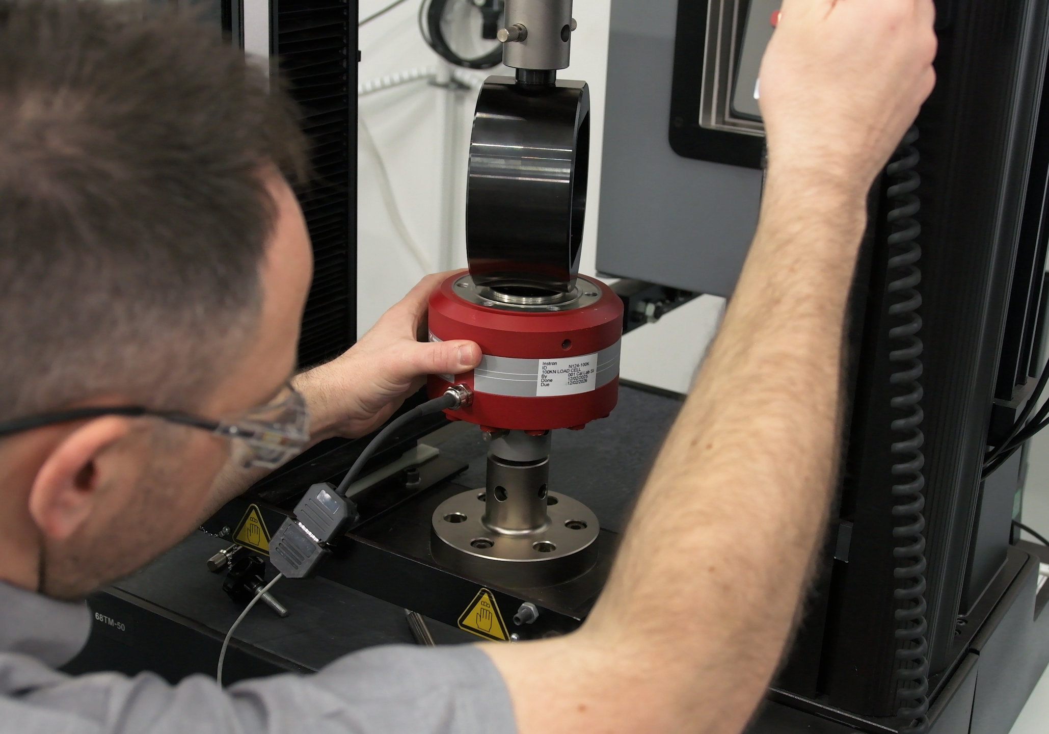 Instron field service engineer aligning a load cell and calibration fixture in a materials testing machine.