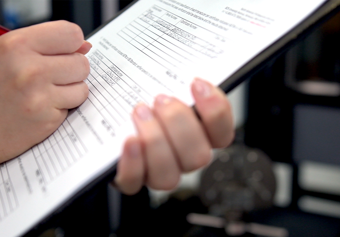 클립보드에 부착된 인쇄된 체크리스트 양식에 빨간 펜으로 글을 쓰는 사람.