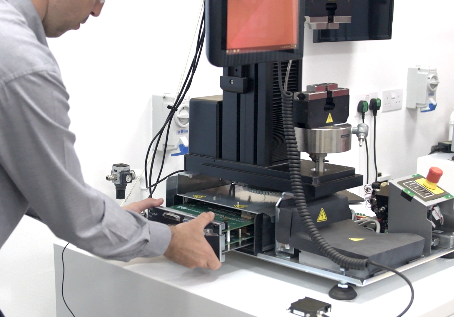 전자 테스트 장비를 작동하며 평가를 위해 회로 기판을 고정 장치에 배치하는 사람.