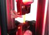 Instron testing system with screw side action grips holding a copper clad laminate strip specimen for tensile testing under red illumination