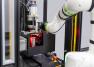 Wide-angle view of a CT6 collaborative robot arm extending into an Instron autoinjector testing machine to load a specimen, with yellow light curtain safety sensors, a discard bin, and an emergency stop button visible in the foreground