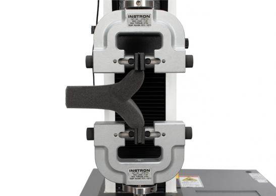 A foam specimen clamped in a pair of Instron screw side-action tensile grips on a universal testing machine performing an ISO 8067 tear strength test of flexible cellular polymeric material