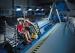 Crash test dummy seated in an automotive seat mounted on an Instron crash simulation sled system with high-speed camera equipment and safety netting visible in the foreground